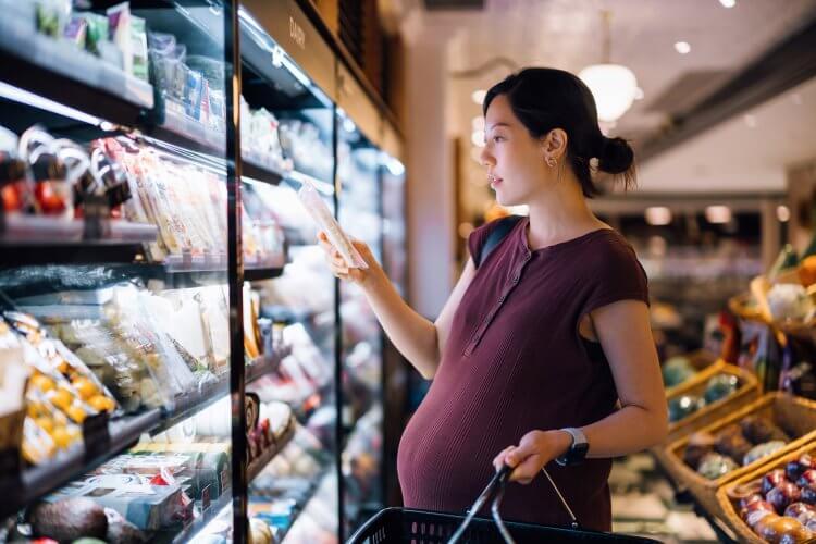 젊은 아시아 임산부는 슈퍼마켓에서 장을 보고 다이어리 통로에서 신선한 치즈를 선택합니다. 균형잡힌 영양으로 잘 먹고 있습니다. 임신 건강 및 웰빙. 임신 중 건강한 식습관과 생활습관